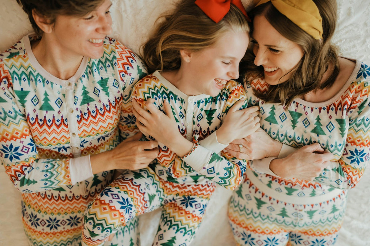 Family laughing together on a bed in matching holiday shirts and pajamas