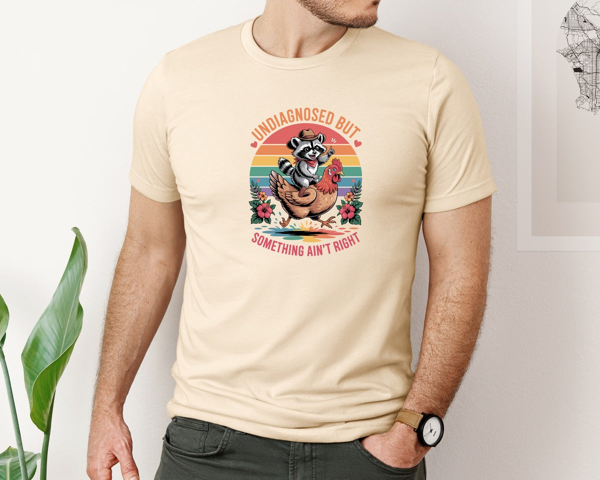 brand:Bella Canvas|color:Soft Cream|Undiagnosed Raccoon Riding Chicken Graphic T-Shirt
