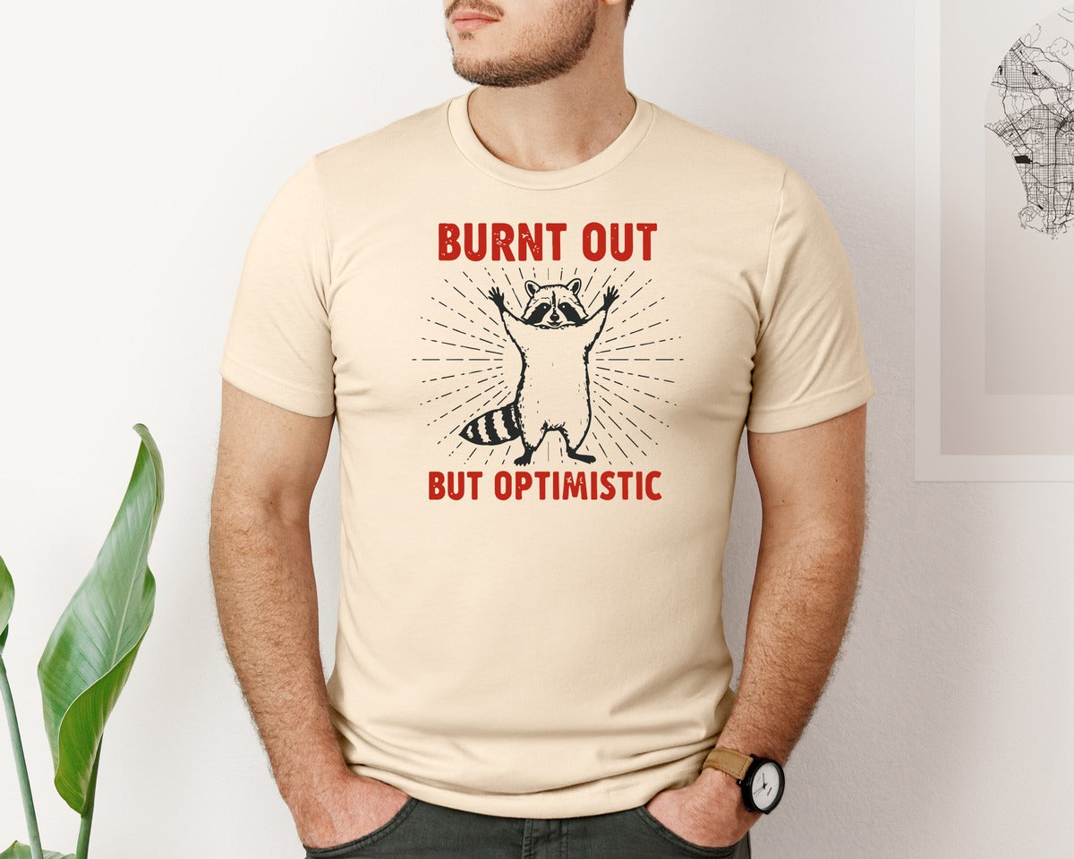 brand:Bella Canvas|color:Soft Cream|Burnt Out But Optimistic Raccoon Graphic T-Shirt